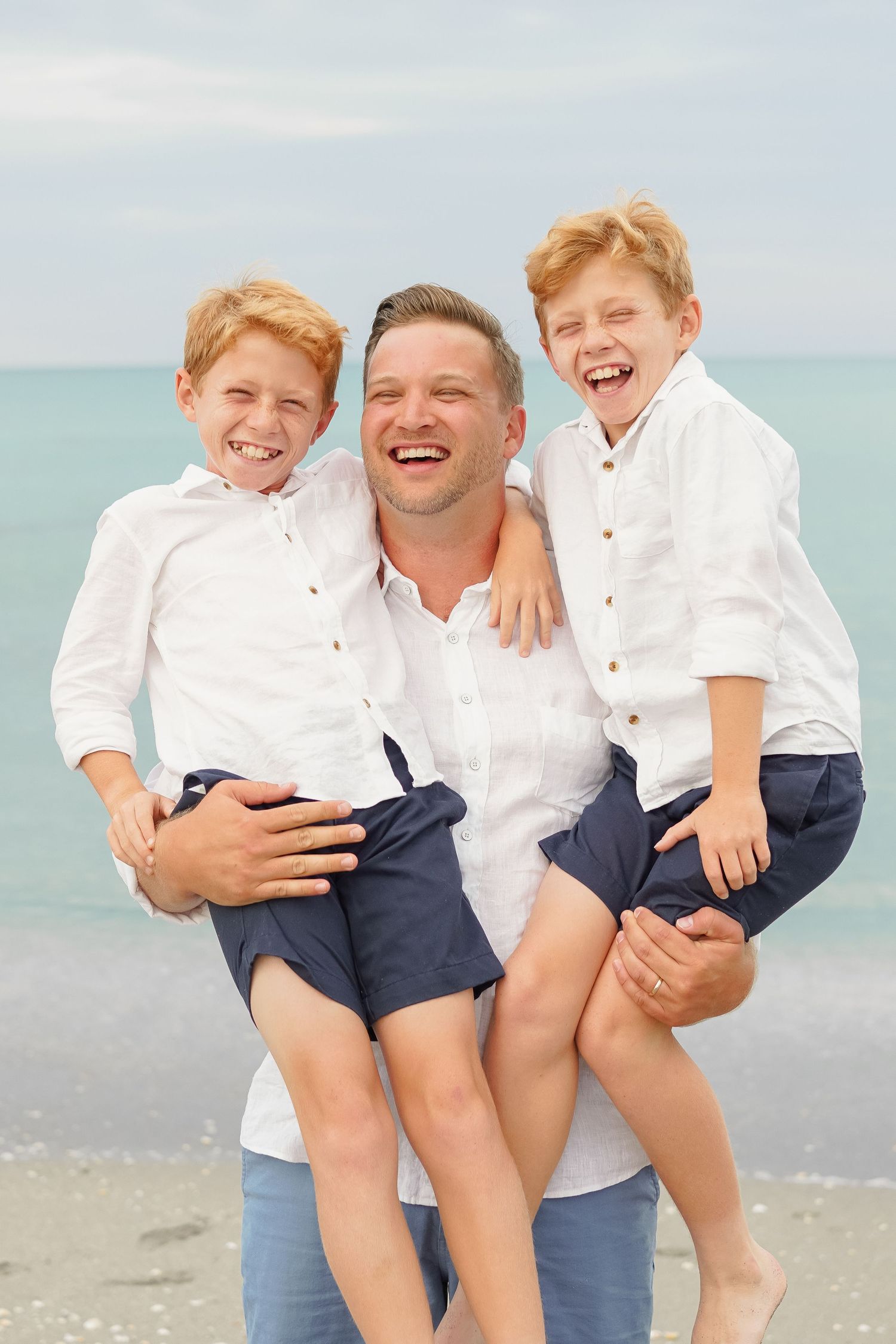 Father holding his two sons at the beach all smiles on the sand