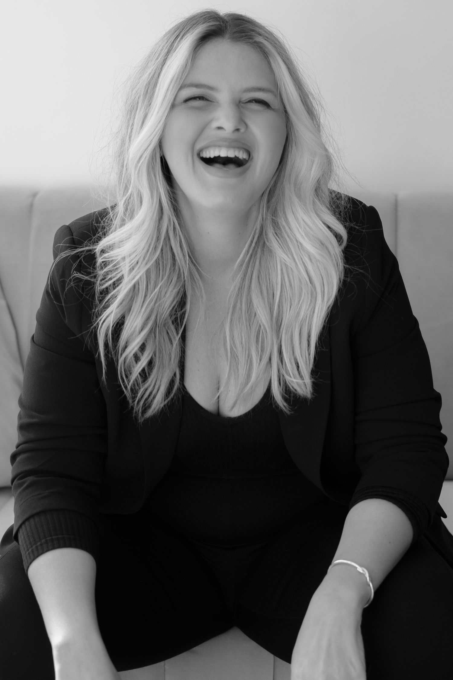 Blonde woman in black outfit smiling and laughing on a couch